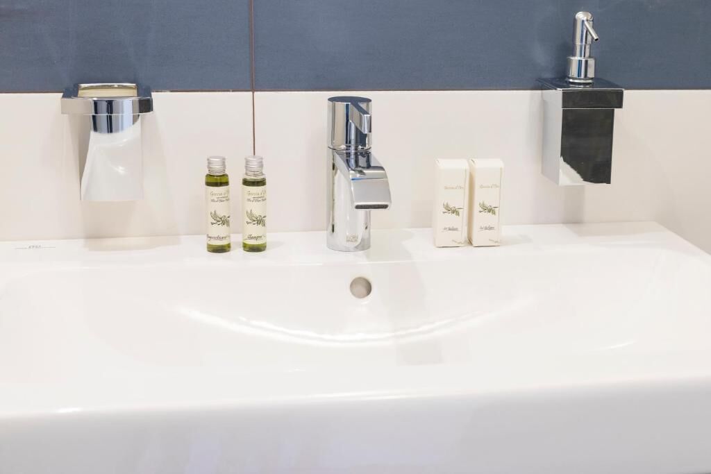 A bathroom sink with two faucets, two soap dispensers, and two bottles of liquid soap.