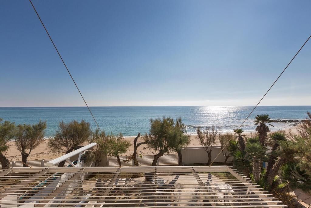 A beach view from a balcony with a railing, palm trees, and a clear sky.