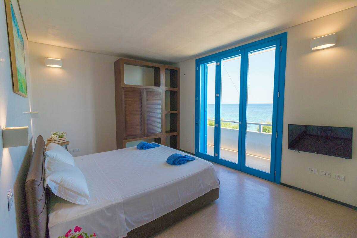 A bedroom with a bed, a TV, a sliding glass door to the outside, and a built-in shelving unit.