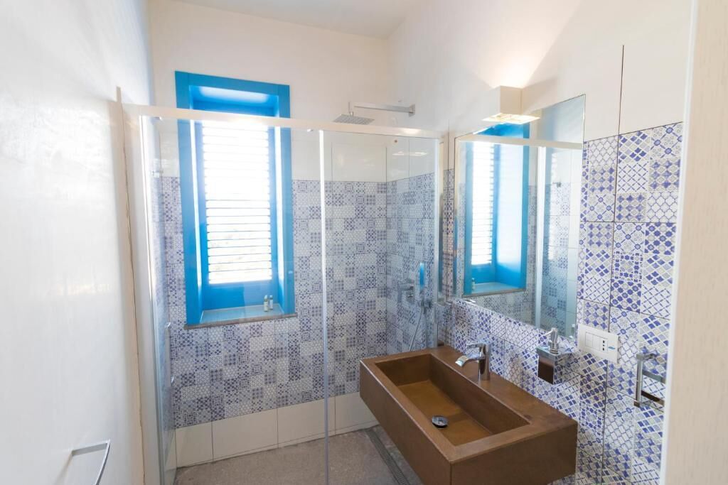 A bathroom with a glass shower enclosure, a wooden sink, and blue-tiled walls.