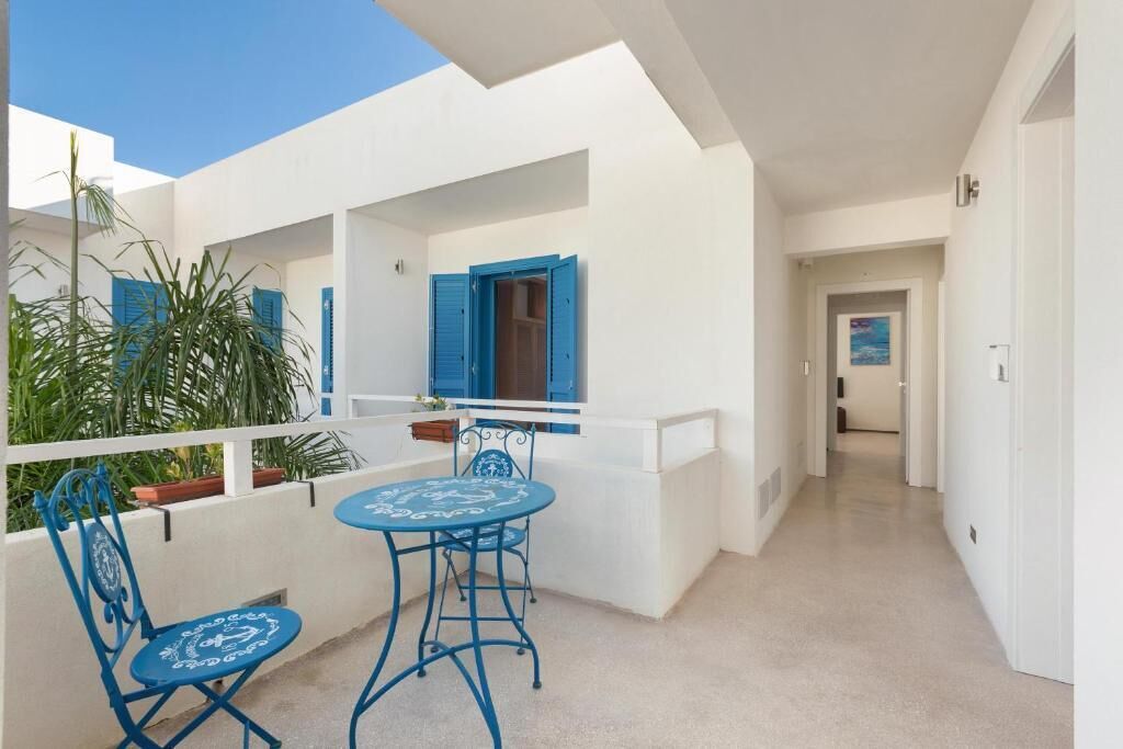 Een balkon met een tafel, stoelen, een bloempot en een blauwe deur.