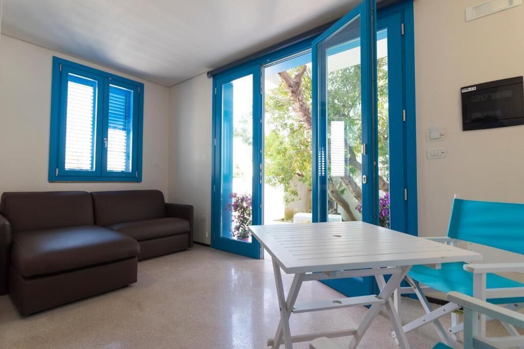 A room with a brown sofa, a white table, and blue-framed doors leading to a garden.