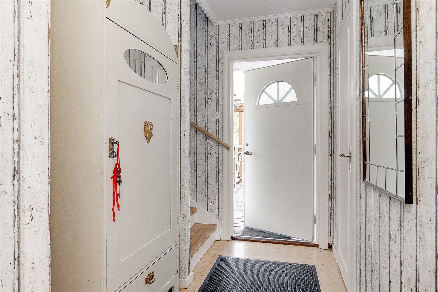 A hallway with a white door, a wooden door frame, a mirror, and a red ribbon on the door.