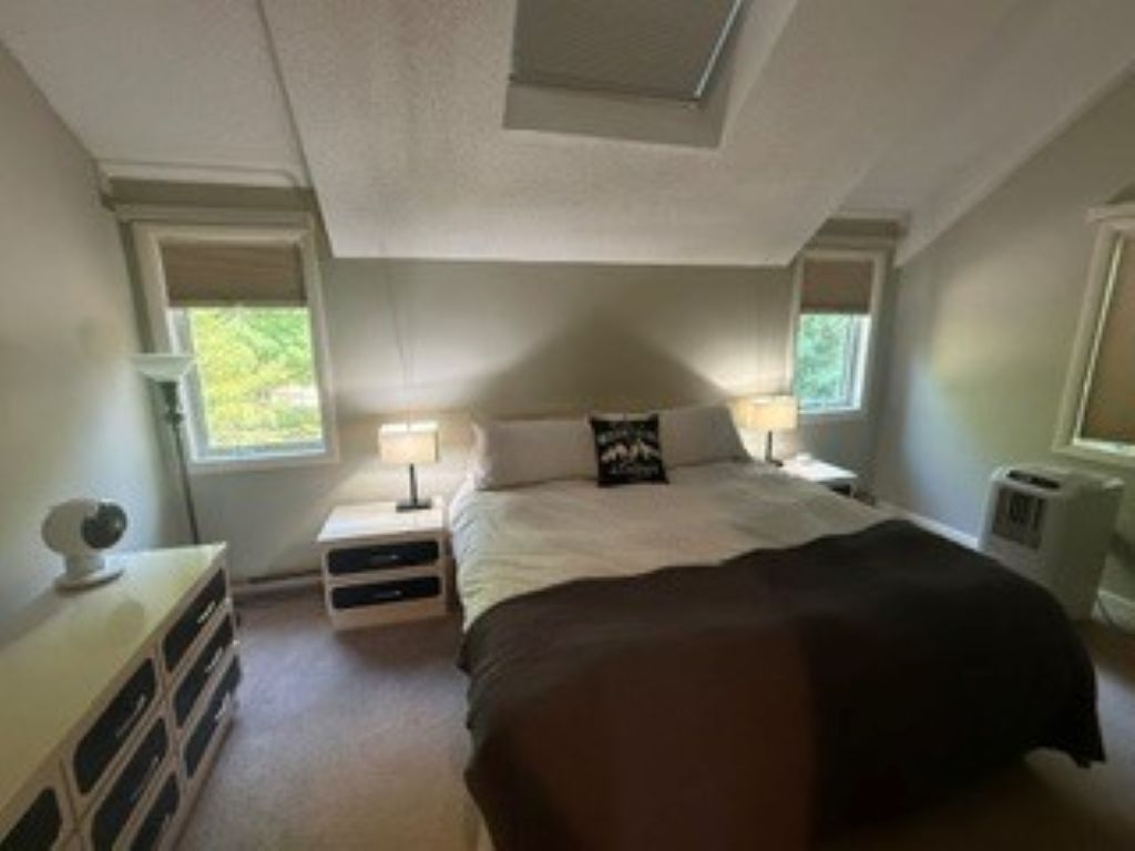 A bedroom with a bed, two bedside tables, a dresser, and a window.