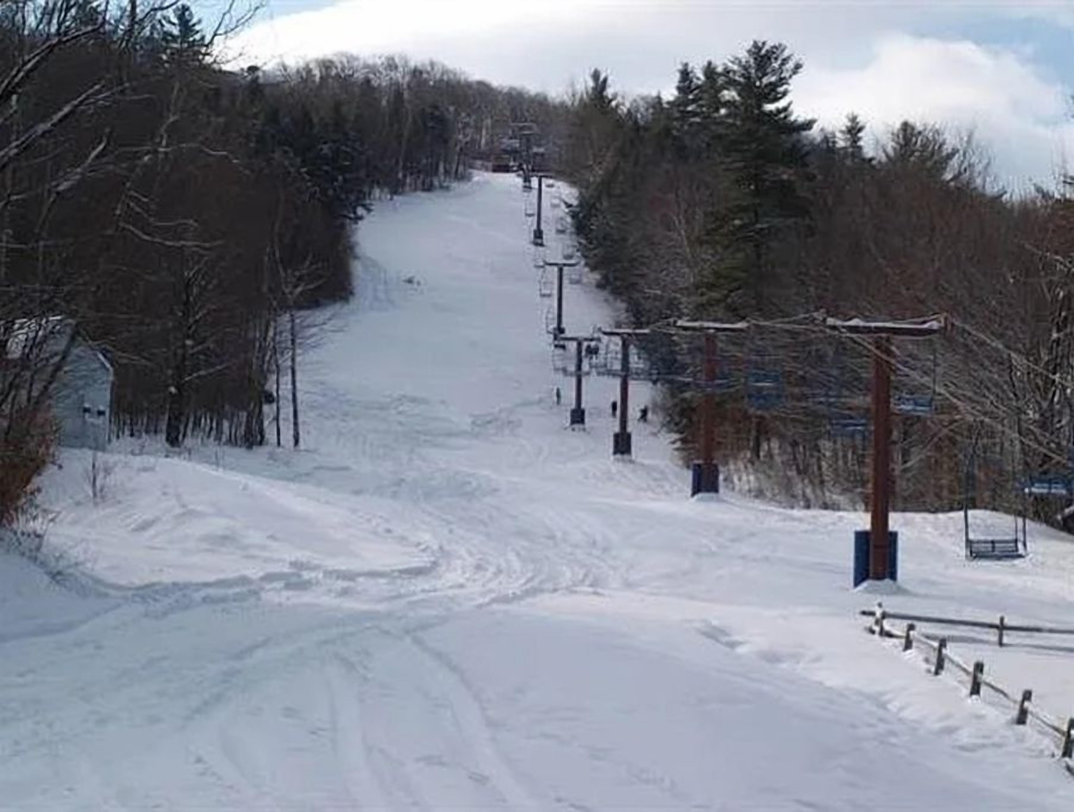 A snowy ski slope with a chairlift, trees, and a clear sky.
