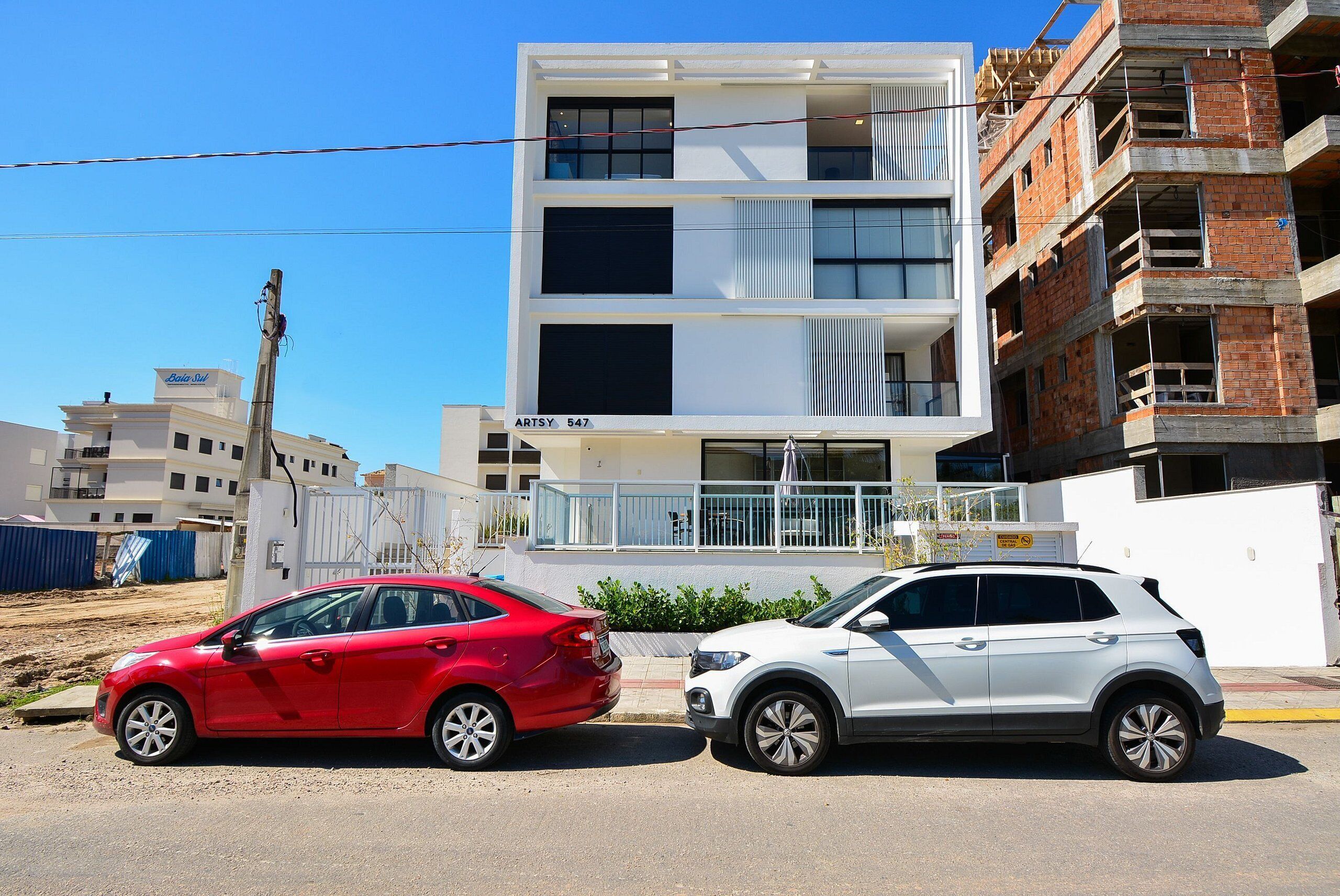 Two cars parked on a street, a building with a sign 'ARTSY 547' in the background, and construction work on the right.