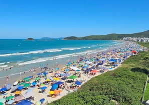 A crowded beach with numerous umbrellas and people enjoying the seaside. - Charme e Conforto - 400m Praia de Palmas (Governador Celso Ramos)