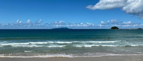Una playa con agua azul cristalina, una orilla arenosa e islas a lo lejos.