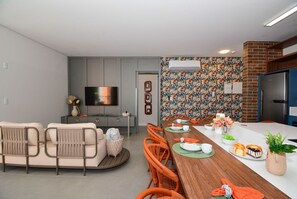 Un soggiorno moderno con divano, poltrone, tavolo da pranzo apparecchiato con piatti e tazze, e televisore.