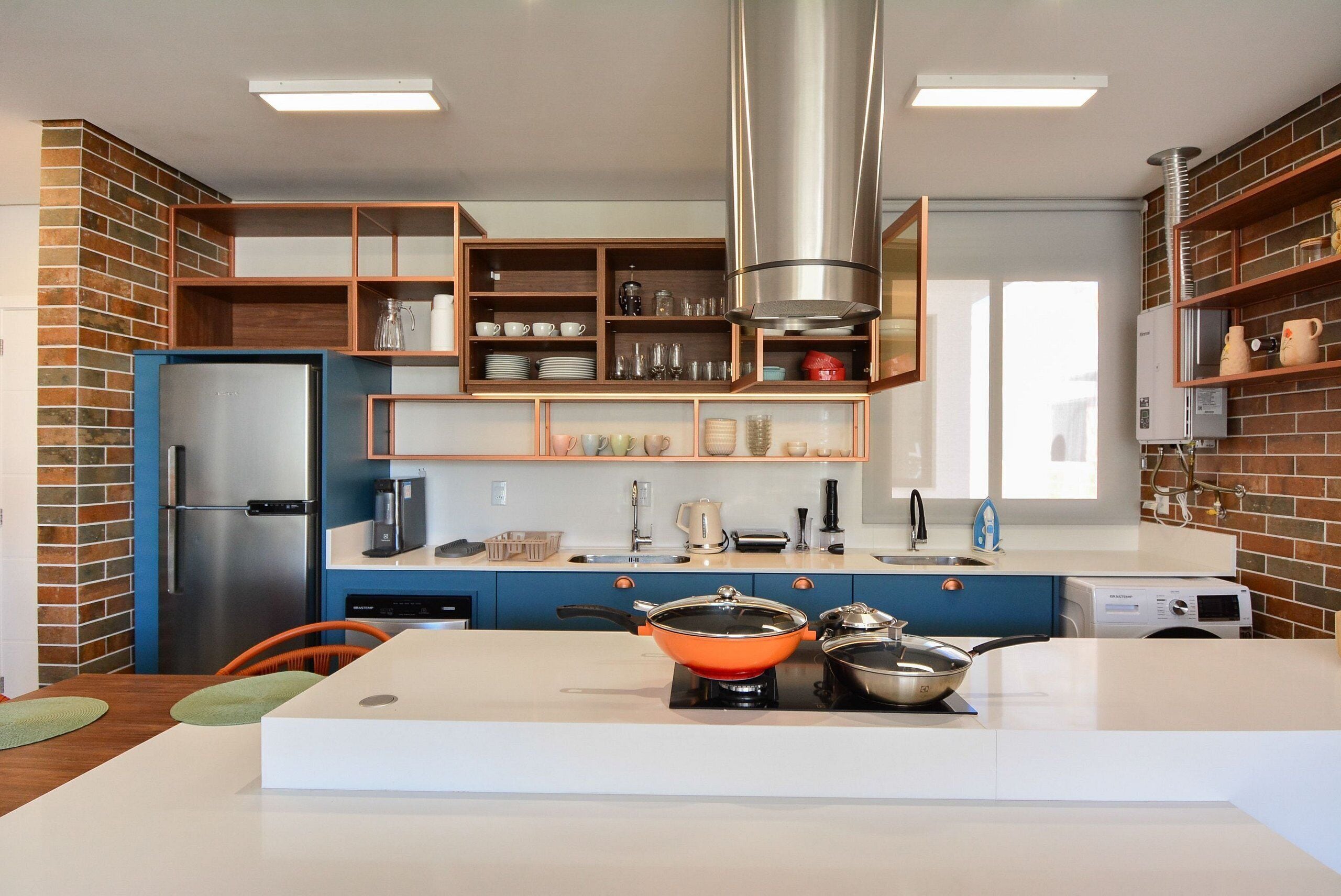 Una cocina moderna con refrigerador empotrado, estufa y repisas con utensilios de cocina.
