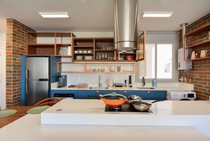 A modern kitchen with a built-in refrigerator, stove, and shelves with kitchenware. - Charme e Conforto - 400m Praia de Palmas (Governador Celso Ramos)