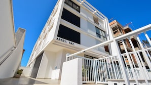 A modern building with a white facade, multiple balconies, and a visible construction site in the background. - Charme e Conforto - 400m Praia de Palmas (Governador Celso Ramos)