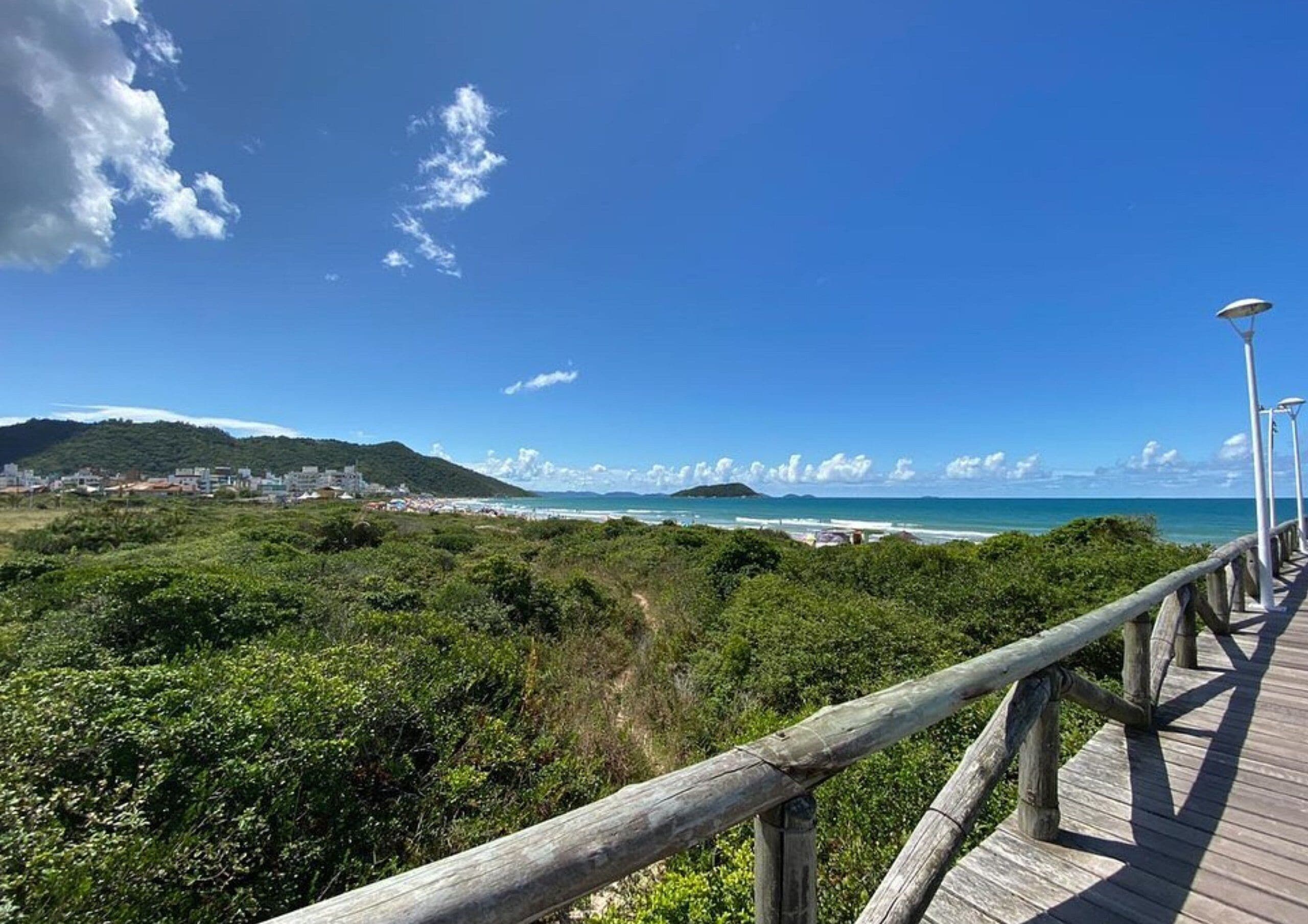 Una pasarela de madera que conduce a una playa, con vista despejada al océano y colinas distantes.