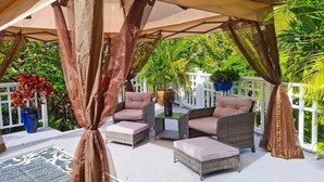 An outdoor patio with wicker furniture, a white fence, and potted plants.