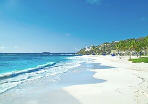 Une plage de sable blanc, avec des vagues et un bâtiment bordé de palmiers.