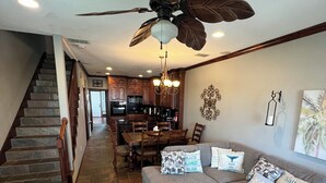 Un salon spacieux avec un canapé gris, un plaid à motifs, un coin repas avec des meubles en bois et un escalier avec des marches en pierre.