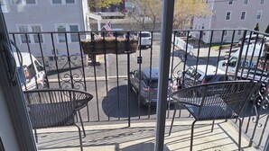 Ein Balkon mit Metallstühlen und Blick auf einen Parkplatz sowie Gebäude im Hintergrund.