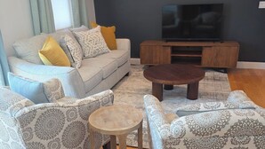 Ein modernes Wohnzimmer mit einer Sofagarnitur, einem Couchtisch und einem Fernseher an einer dunklen Wand.