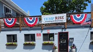 A building with a sign that reads 'TEMP RISE Cooling & Heating.' There are American flags and a banner with stars and stripes. The building has a wooden balcony with railings.