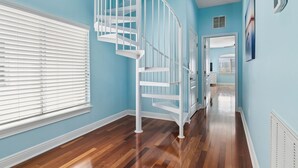 Un pasillo con una escalera espiral blanca, suelo de madera y paredes azul claro.