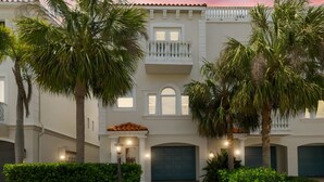 Un edificio de dos pisos con balcón, garaje y palmeras.