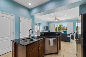 A modern kitchen with a black countertop, stainless steel appliances, and a view to the living area. - Jazzy's Waterfront Cove w/ Heated Pool & Rooftop, Walk to the Beach (Clearwater)