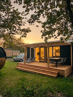 A wooden deck with a covered seating area, a car parked nearby, and a building with a glass door.