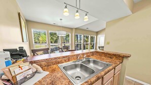 A kitchen with granite countertops, a stainless steel sink, and a window overlooking a balcony. - Luxury Condo with Golf Course Views, Pools & Resort Access! (New Bern)