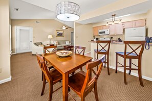 A dining area with a wooden table and chairs, a ceiling fan, and a kitchen in the background. - Luxury Condo with Golf Course Views, Pools & Resort Access! (New Bern)