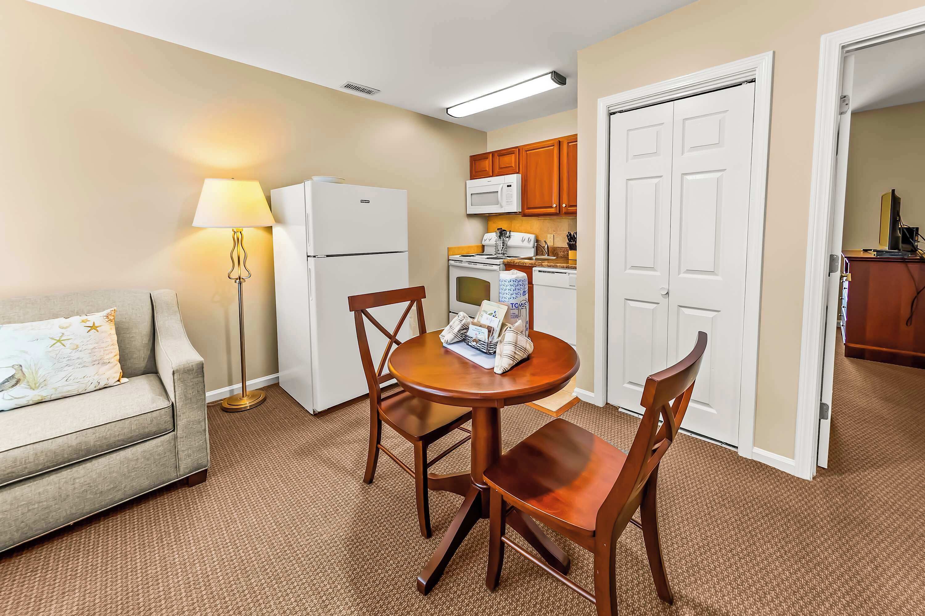 A compact living space with a kitchenette, a dining area with a table and chairs, a sofa, and a lamp.