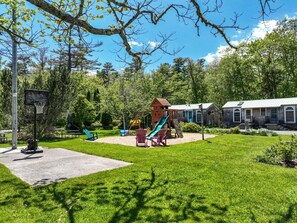 Ein Spielplatz mit Rutsche, Schaukeln und einem Basketballkorb.