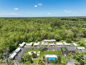 Eine Vogelperspektive zeigt einen Campingplatz mit mehreren Holzhütten, einem Schwimmbad und einem großen Gebäude mit grüner Dachbegrünung.