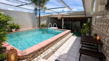 A swimming pool with a stone border, a wooden deck, and potted plants.
