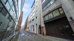 En smal stadsgata med moderna byggnader, en asfalterad trottoar och en klar himmel.