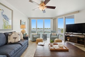 A living room with a sofa, two armchairs, a coffee table, a TV, and a balcony with a view. - Seaspray Riverside 312 (Pensacola)