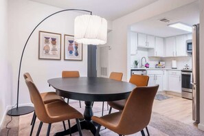 Eine moderne Küche mit weißen Schränken, einem Edelstahl-Kühlschrank und einem Essbereich mit rundem Tisch und braunen Stühlen.