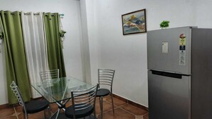 Eine kleine Küche mit einem Glastisch, zwei Stühlen, einem Kühlschrank und einem Bild an der Wand.