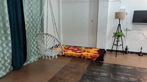 Ein Zimmer mit Hängekorbsessel, einem Bett mit floralem Überwurf, einem Topfpflanzen, einer Lampe und einem Fernseher an der Wand.
