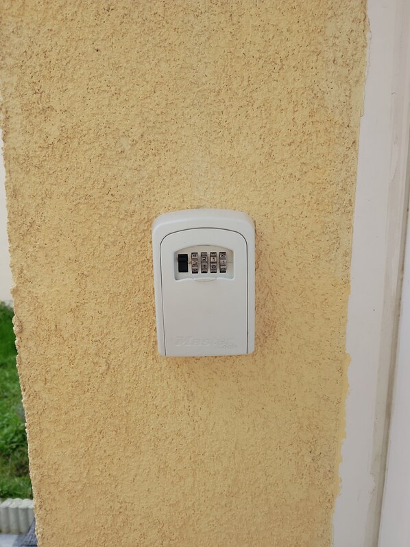 A white security keypad mounted on a textured beige wall.