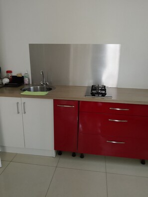 Une cuisine équipée d’un évier en acier inoxydable, d’une cuisinière à gaz et d’un meuble de rangement rouge et blanc.