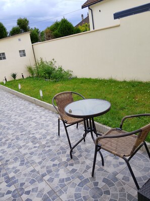 A patio with a round table and two wicker chairs, surrounded by a patterned tile floor.
