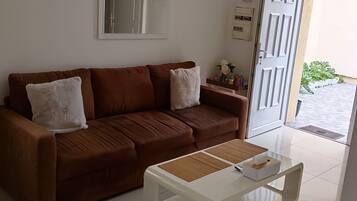 Un salon avec un canapé marron, une table basse blanche et une porte donnant sur l’extérieur.