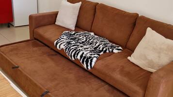 A brown sofa with a zebra-patterned throw blanket and two pillows, a white cabinet, and a microwave on top of a white refrigerator.