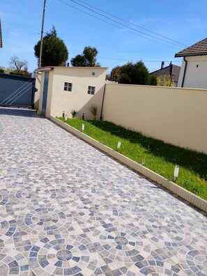 Un camino pavimentado con un diseño geométrico de baldosas, bordeado por un muro bajo y una zona verde con pequeñas plantas.