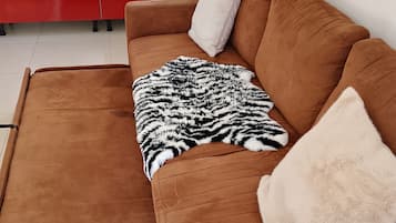Een bruine bank met een zwart-wit deken en twee kussens, een rode kast en een witte koelkast in een kamer met witte muren en een raam.