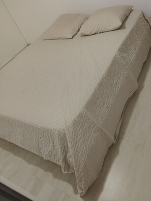 A bed with a textured beige cover and two pillows.