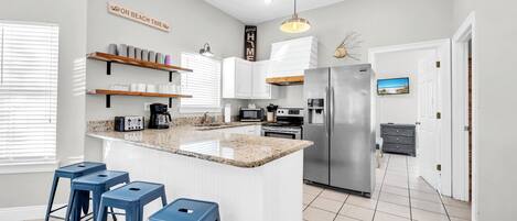 A modern kitchen with a central island, bar stools, built-in appliances, and a view of the living area.