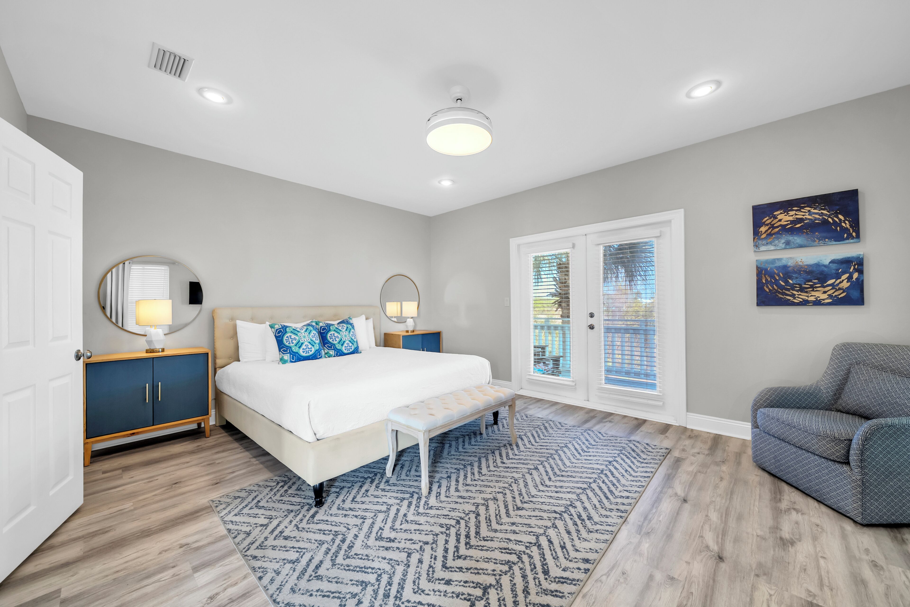 A bedroom with a bed, bedside tables, a bench, a sofa, and a view of the outside.
