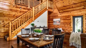 A wooden interior with a dining area, staircase, and a window with a view. - Indoor Pool + Arcade Loft | 4 En-Suite BRs | Gated Bear Crossing Cabin (Sevierville)