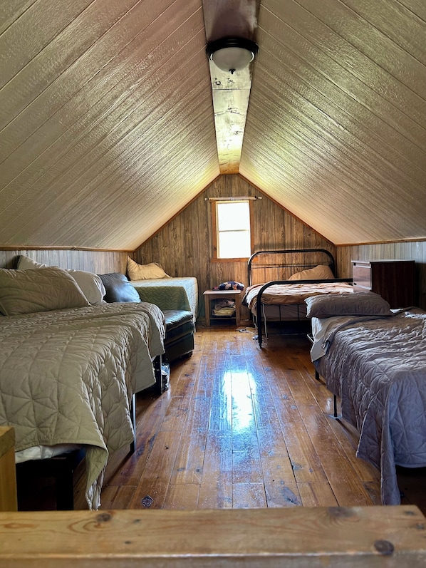 Dormitorio tipo loft con dos camas, una mesita y un ventanal.